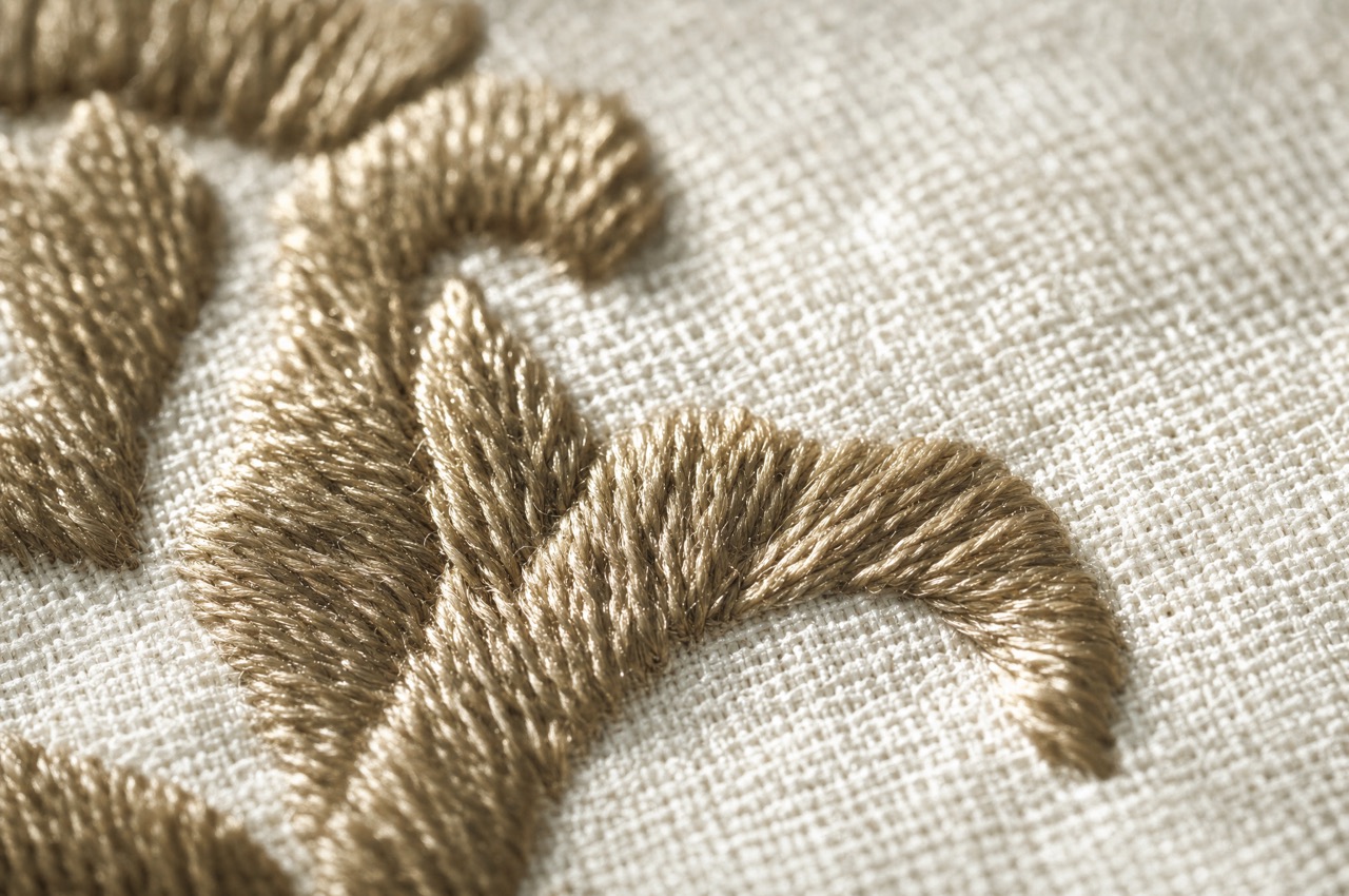 An extreme close-up of a satin-stitched edge, the thread laid in tight parallel rows catching the light.