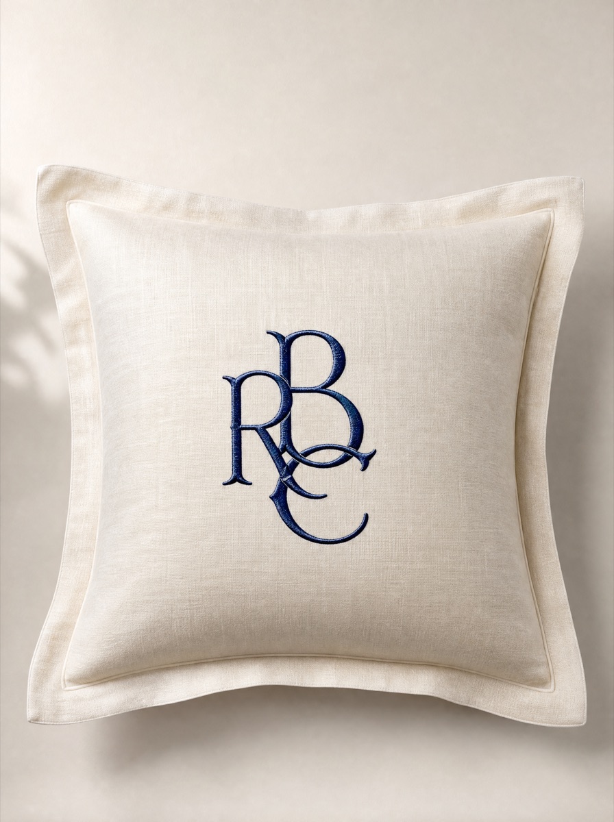 A 20-inch ivory pillow sham with a navy satin-stitched monogram centered on the front.
