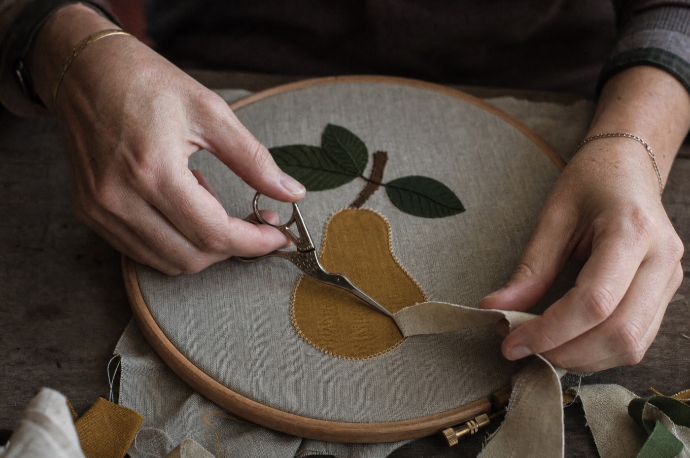 Hands trimming an appliqué shape free with small scissors before the satin edge is stitched.